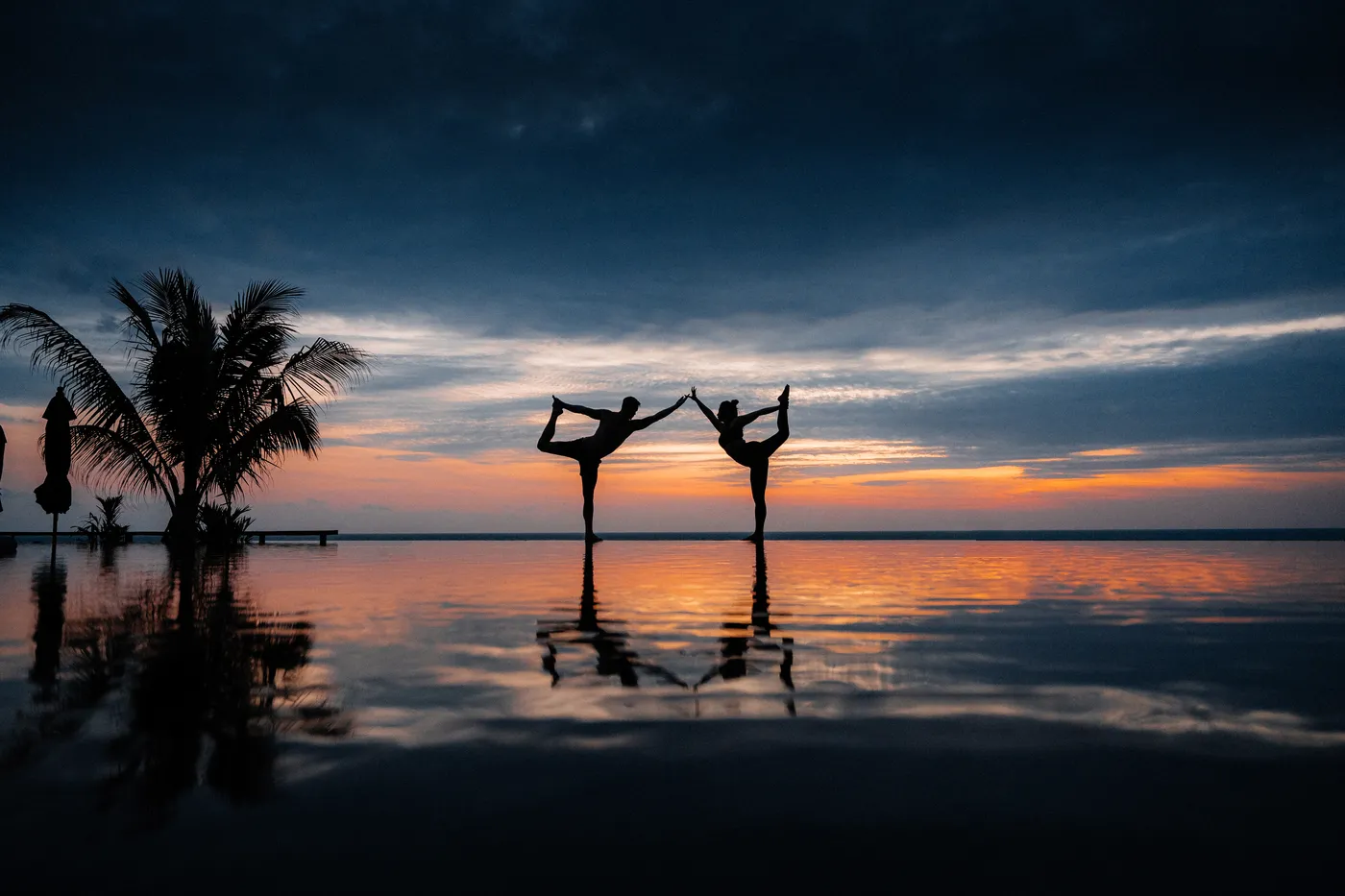 Silhuetas fazendo yoga ao pôr do sol sobre a piscina de borda infinita